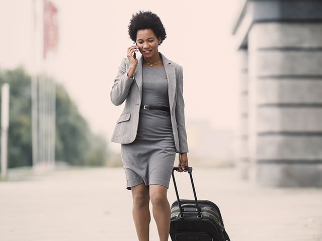Woman on business travel talking on phone while holding suitcase